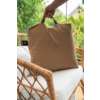 Hand houdt een beige kussen met handgreep vast op een rotanstoel met wit zitkussen, planten en een huisdak op de achtergrond
