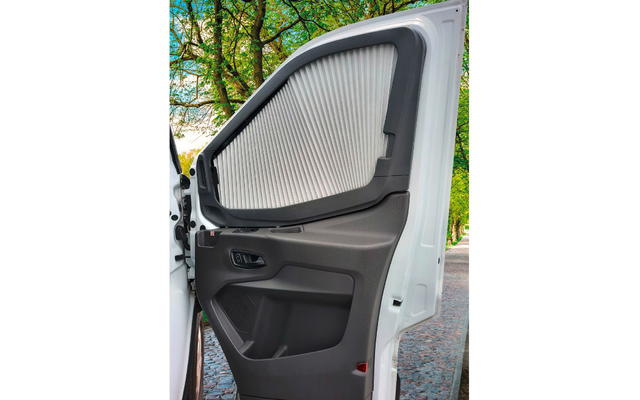 Geöffnete weiße Fahrzeugtür, graue Innenverkleidung, gefaltete Abdeckung vor der Seitenscheibe, Türgriff, Ablagefach, roter Reflektor; im Hintergrund Bäume und Weg