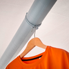 Oranges T‑Shirt auf einem Holzkleiderbügel, der mit einer Schnur an einem grauen Rohr hängt