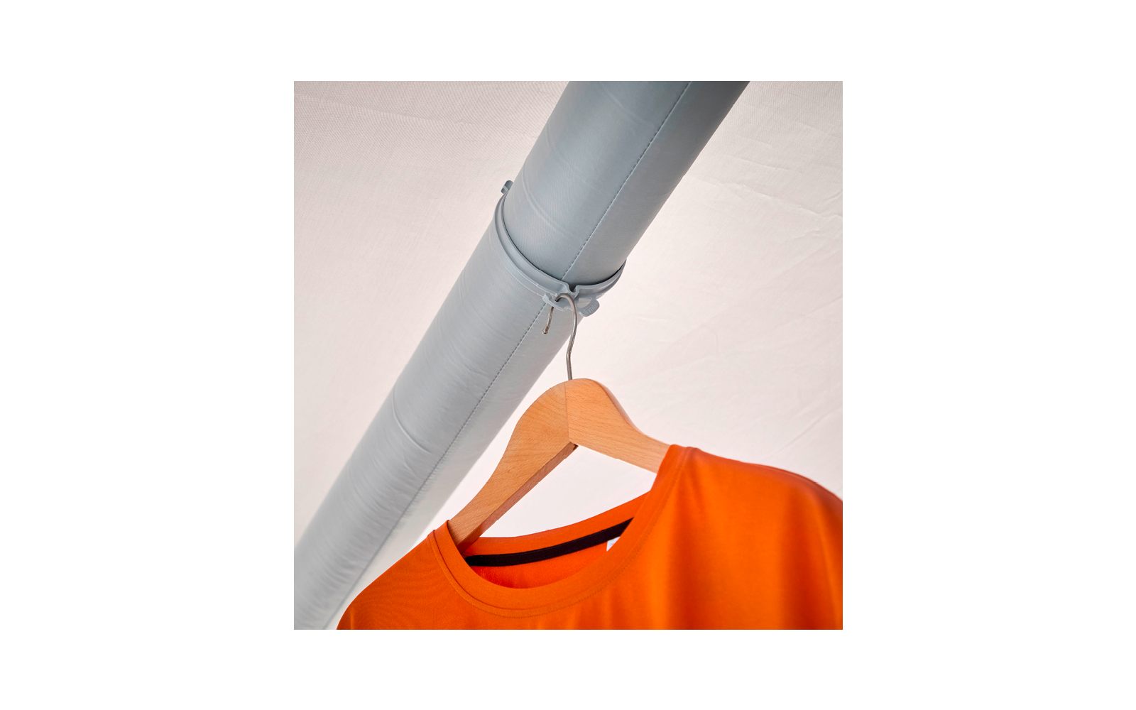 Oranges T‑Shirt auf einem Holzkleiderbügel, der mit einer Schnur an einem grauen Rohr hängt