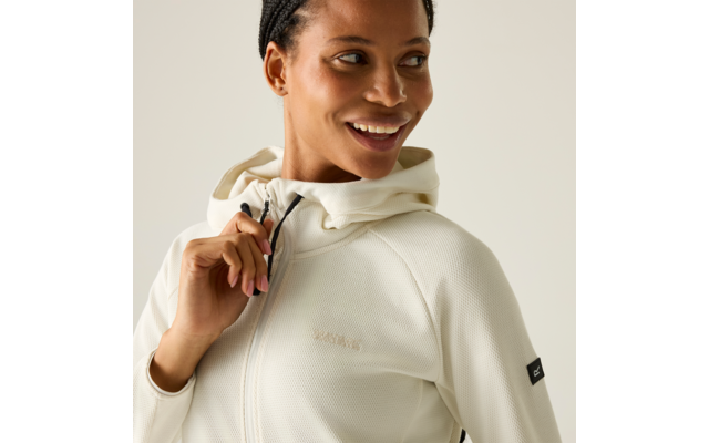 Lächelnde Person in weißem Kapuzen-Zip-Pullover hält Kordel, Blick zur Seite, neutraler Hintergrund