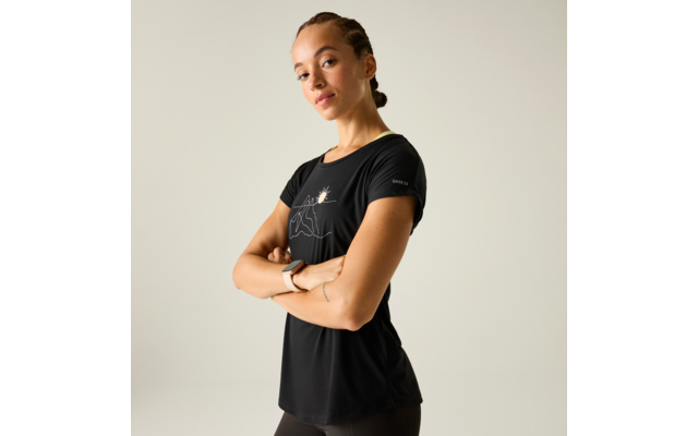 Person leicht gedreht vor hellem Hintergrund, Arme vor der Brust verschränkt, trägt schwarzes T‑Shirt mit weißer Liniengrafik (Berg und Sonne), geflochtenes Haar zusammengebunden, Armbanduhr am linken Handgelenk