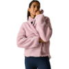 Persoon met roze fleecejas met hoge kraag en donkerblauwe legging voor een effen lichte achtergrond, één hand raakt de kraag, kijkt omhoog en opzij