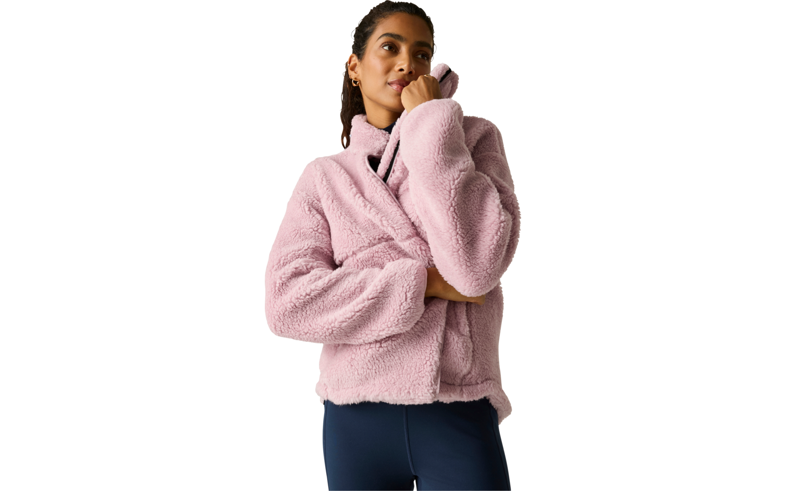 Persoon met roze fleecejas met hoge kraag en donkerblauwe legging voor een effen lichte achtergrond, één hand raakt de kraag, kijkt omhoog en opzij