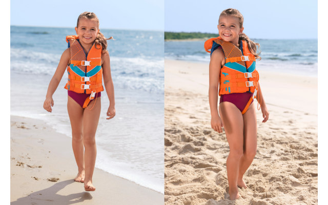 Junges Mädchen mit orangefarbener Rettungsweste und roter Badebekleidung läuft am Sandstrand, Meer im Hintergrund