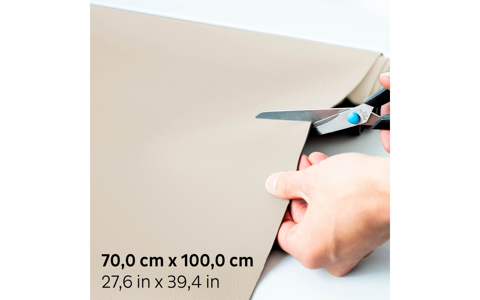 Deux mains coupent un matériau beige avec des ciseaux sur fond blanc ; en coin, dimensions noires 70,0 cm x 100,0 cm et 27,6 in x 39,4 in visibles
