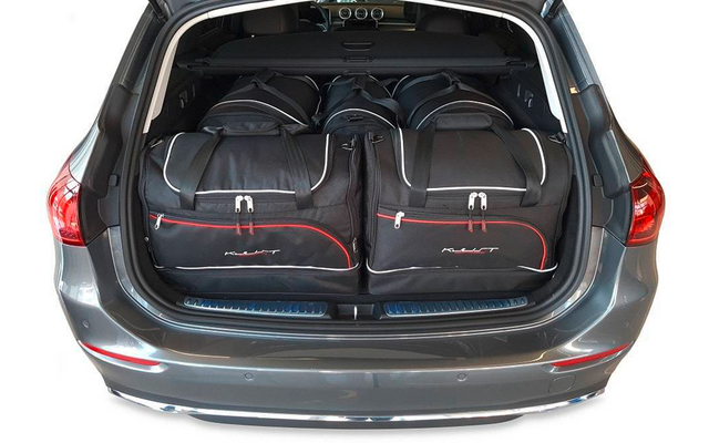 Coffre ouvert d'une voiture grise contenant quatre sacs de voyage noirs avec liserés rouges et blancs