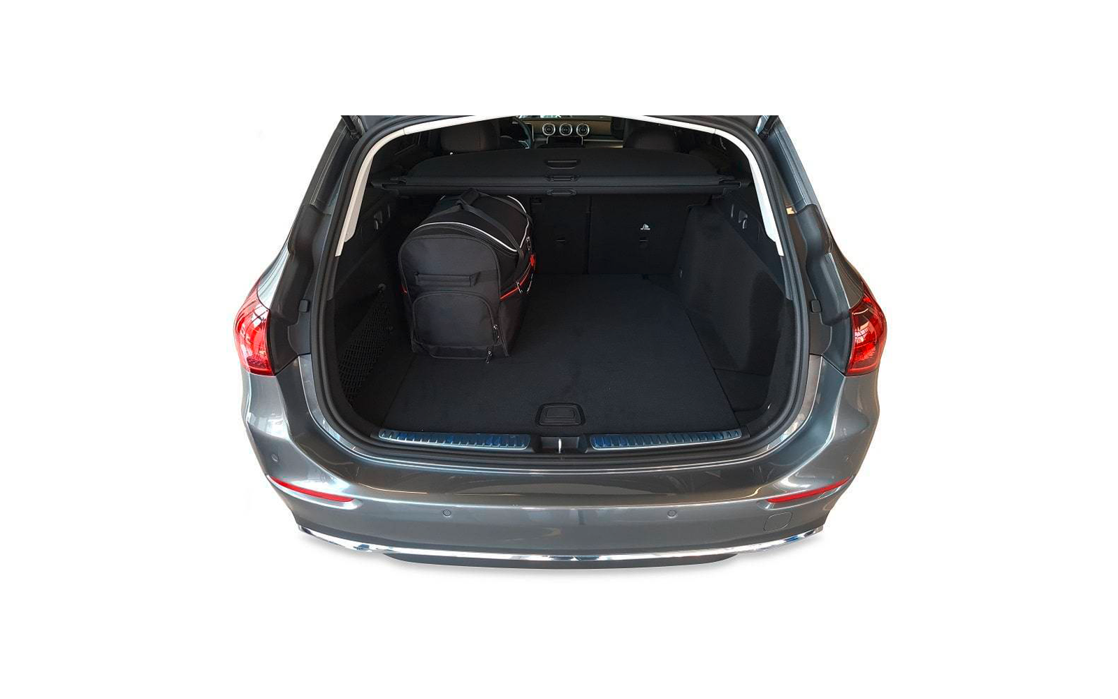 Coffre ouvert d'une voiture grise, sac noir à gauche, tapis sombre, cache-bagages rétractable visible