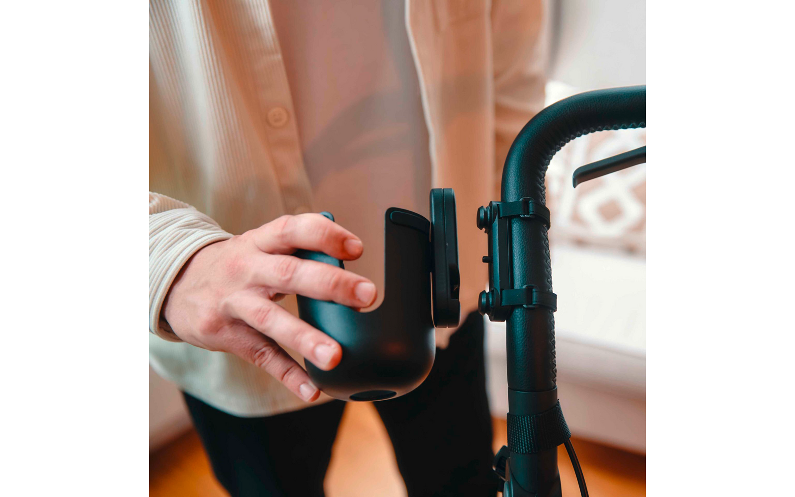 Hand befestigt schwarze Halterung mit Klemme an gebogenem schwarzen Griff, unscharfer Hintergrund mit Sofa