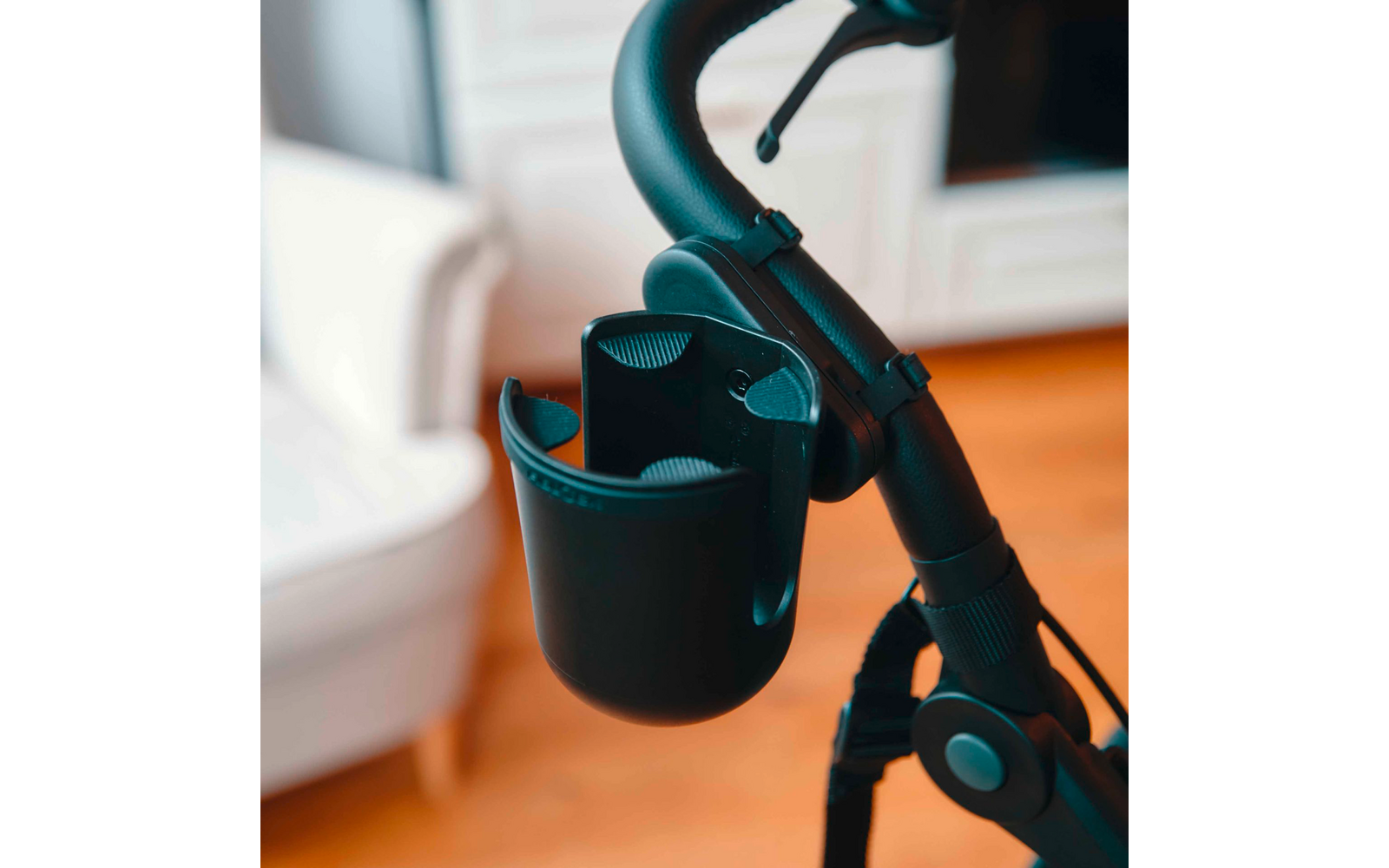 Schwarzer Griff mit befestigtem schwarzem Becherhalter, unscharfer weißer Sessel und Holzfußboden im Hintergrund