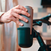 Hand hält einen grauen Thermobecher über einem schwarzen Becherhalter am Fahrradlenker