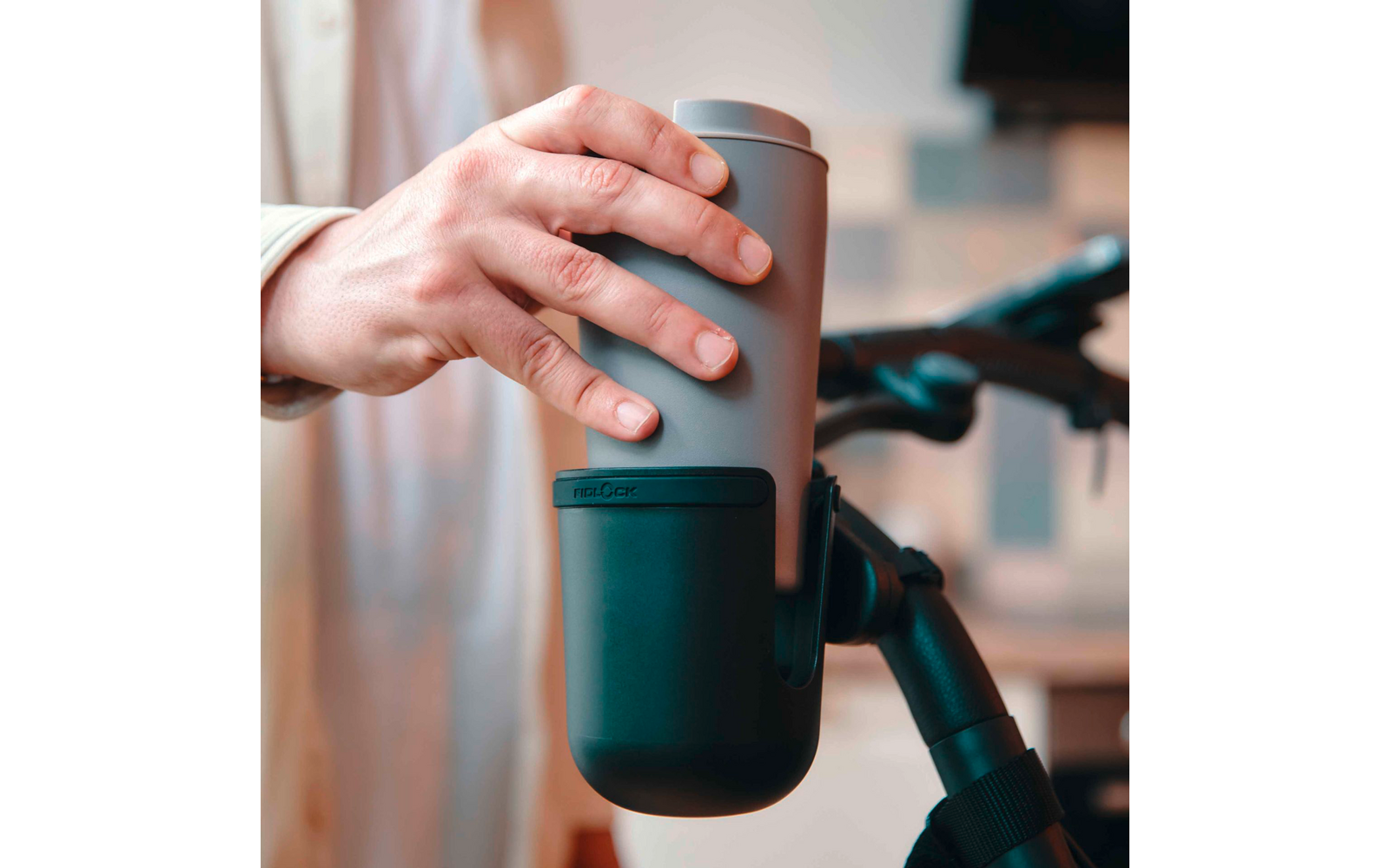 Hand hält einen grauen Thermobecher über einem schwarzen Becherhalter am Fahrradlenker