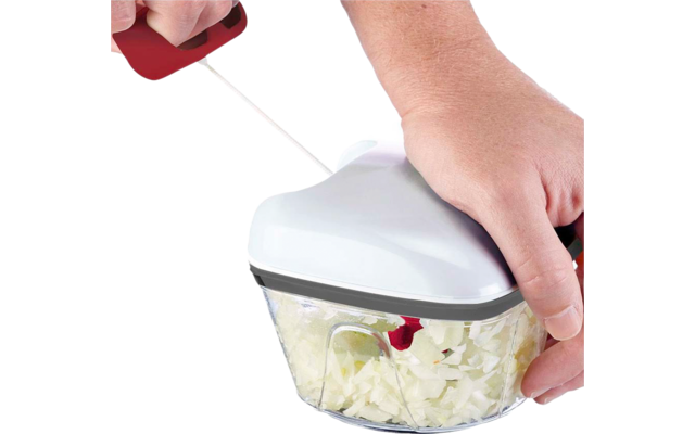 Deux mains utilisent un hachoir manuel avec couvercle blanc ; le bol transparent contient de petits morceaux blancs hachés ; une main tire sur une poignée rouge à cordon