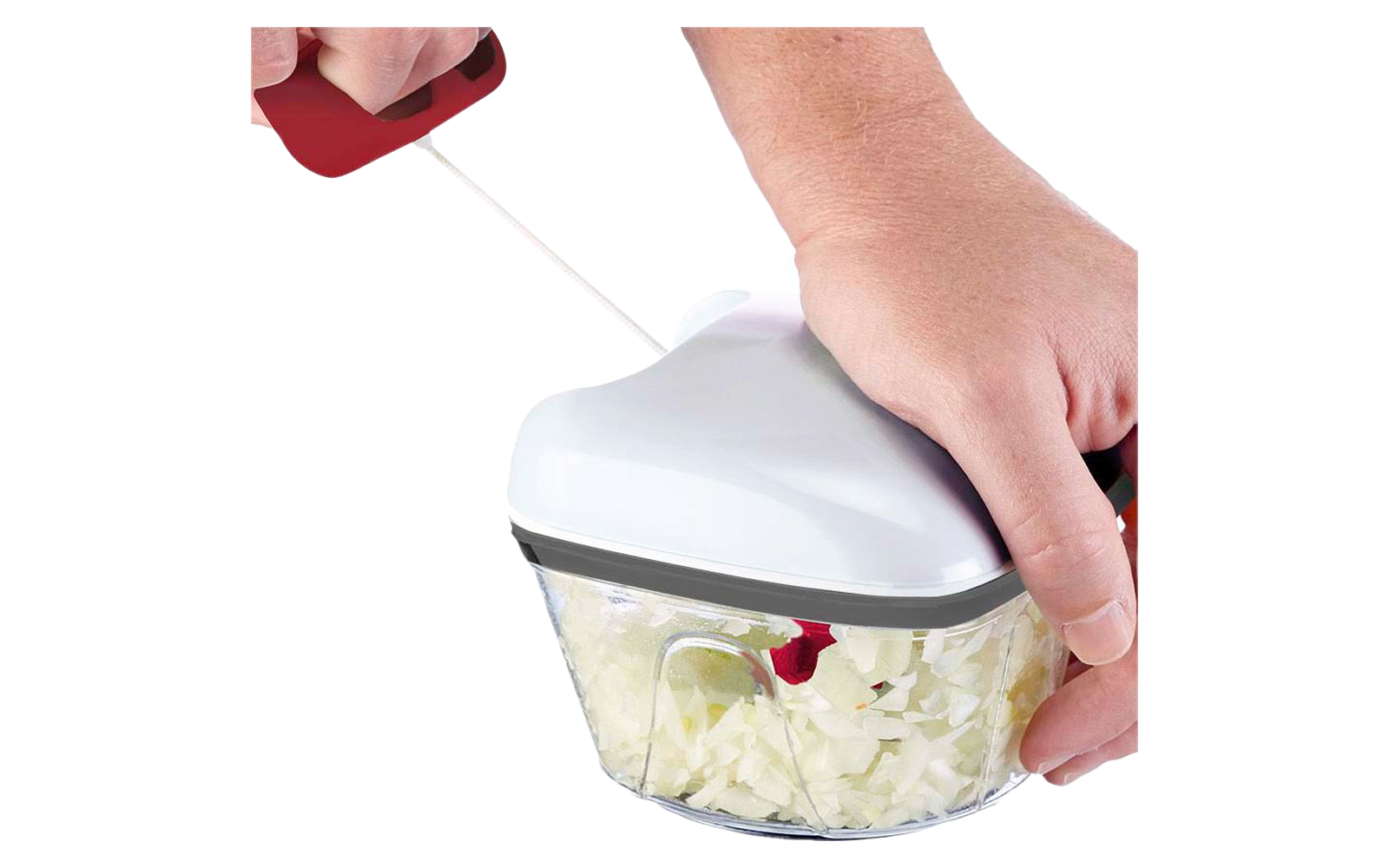 Deux mains utilisent un hachoir manuel avec couvercle blanc ; le bol transparent contient de petits morceaux blancs hachés ; une main tire sur une poignée rouge à cordon