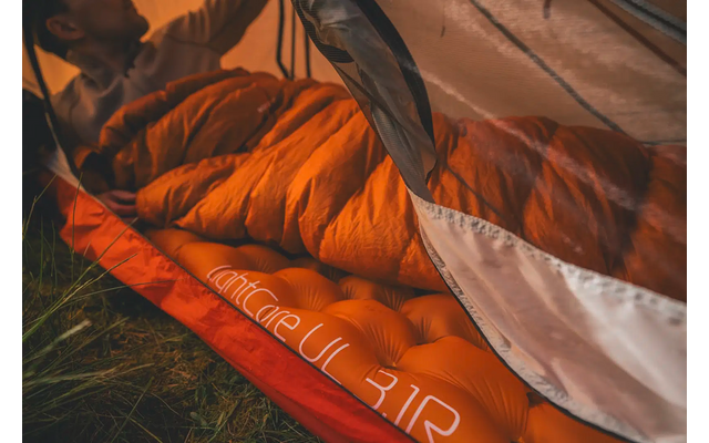 Tent met open ingang en oranje binnentent, persoon liggend met bruine schoenen