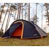 Tent on grass in the forest, tall trees surround the tent, blue sky visible