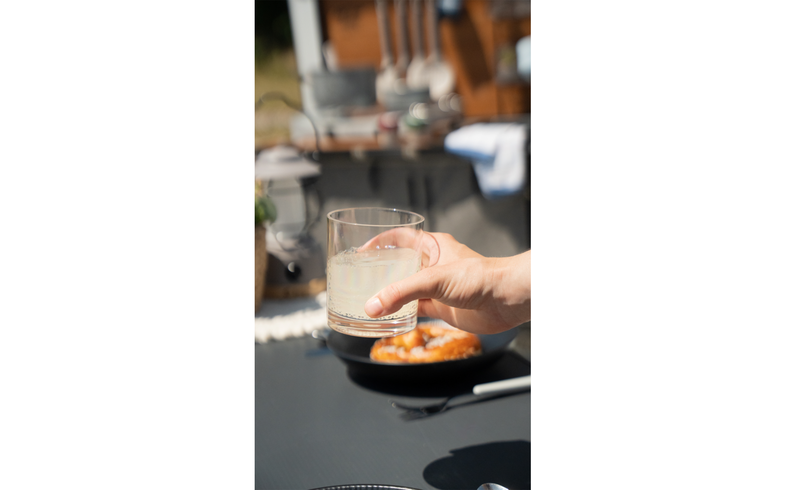 Hand houdt een glas met drankje boven een bord met eten op een tafel