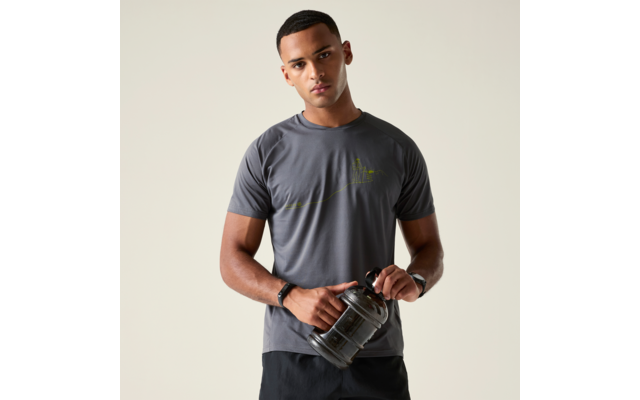 Mann mit kurzen Haaren in grauem T-Shirt und dunklen Shorts hält eine große schwarze Trinkflasche vor hellem Hintergrund
