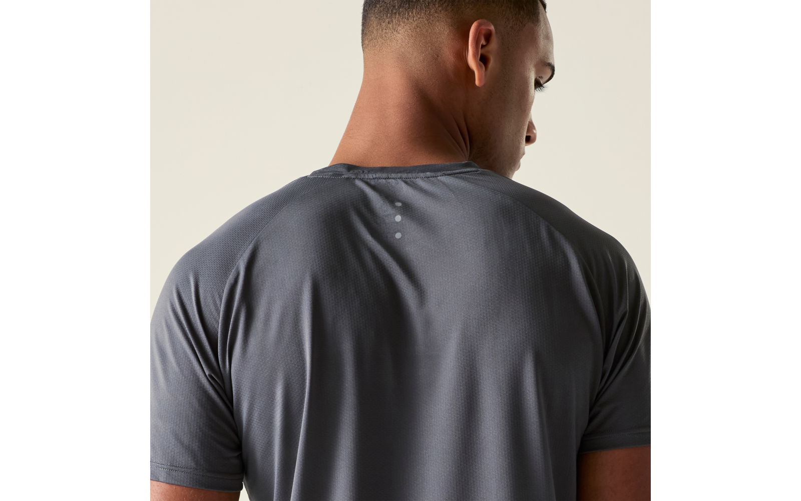 Rückenansicht einer Person mit kurzem Haar, graues T-Shirt, heller Hintergrund