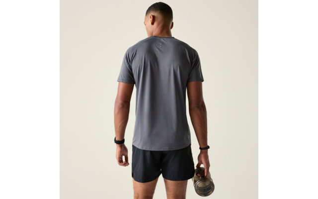 Person von hinten in grauem T-Shirt und schwarzen Shorts, hält eine Kettlebell in der rechten Hand vor beigem Hintergrund