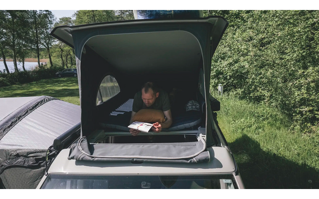 Mann liest in einem Auto mit offenem Dachzelt in der Natur