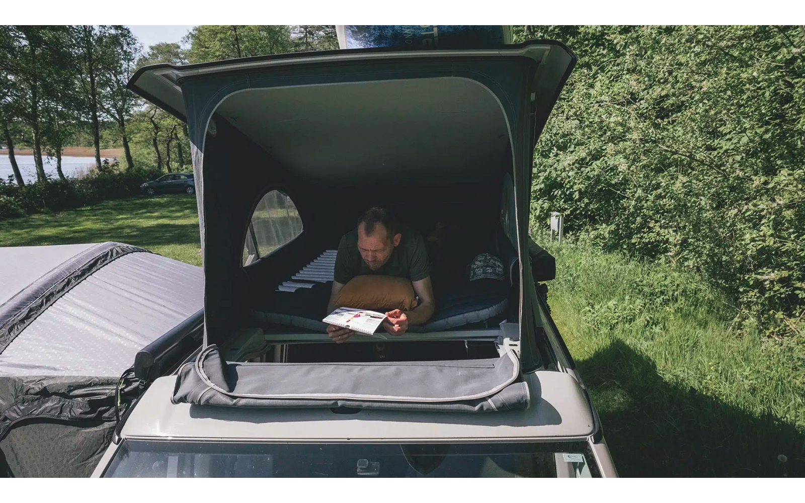Mann liest in einem Auto mit offenem Dachzelt in der Natur