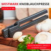 Presse à ail grise en métal sur une planche en bois, avec gousses d'ail, deux têtes d'ail et du persil ; bandeau rouge en haut avec l'inscription 'WESTMARK KNOBLAUCHPRESSE' et indication de taille, encart rouge en bas à droite avec texte