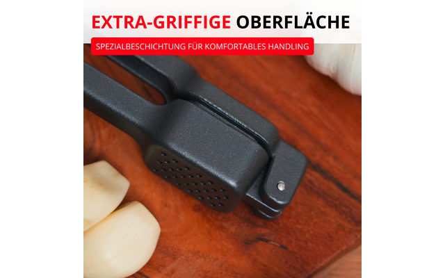 Presse à ail noire sur planche en bois, deux gousses d'ail épluchées à gauche, bandeau rouge en haut avec texte blanc EXTRA-GRIFFIGE OBERFLÄCHE et texte plus petit SPEZIALBESCHICHTUNG FÜR KOMFORTABLES HANDLING