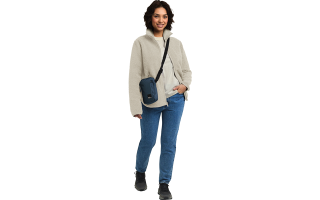 Frau steht, trägt helle Jacke, blaue Jeans und schwarze Tasche über der Schulter