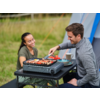 Zwei Personen grillen gemeinsam im Freien, eine Frau und ein Mann, der mit einer Zange Würstchen auf dem Grill wendet