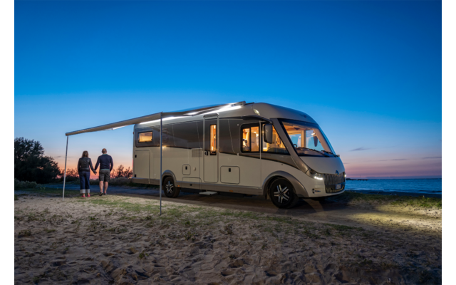 Autocaravana estacionada en un campo abierto al atardecer con dos personas al lado