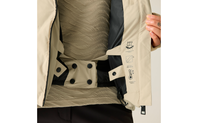 Geöffnete beige Jacke, schwarzes Innenfutter und Steppung sichtbar, Innengurt mit Druckknöpfen, Innenklappe mit Funktions- und Pflegepiktogrammen, beigefarbener gewellter Pullover darunter, Hand mit gelbem Nagellack hält die Jacke