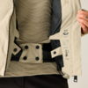 Geöffnete beige Jacke, schwarzes Innenfutter und Steppung sichtbar, Innengurt mit Druckknöpfen, Innenklappe mit Funktions- und Pflegepiktogrammen, beigefarbener gewellter Pullover darunter, Hand mit gelbem Nagellack hält die Jacke