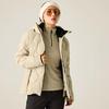 Person trägt beigefarbene Steppjacke, hellen Pullover mit kurzem Reißverschluss, beigefarbene Mütze, Sonnenbrille und dunkle Hosen vor hellem einfarbigen Hintergrund