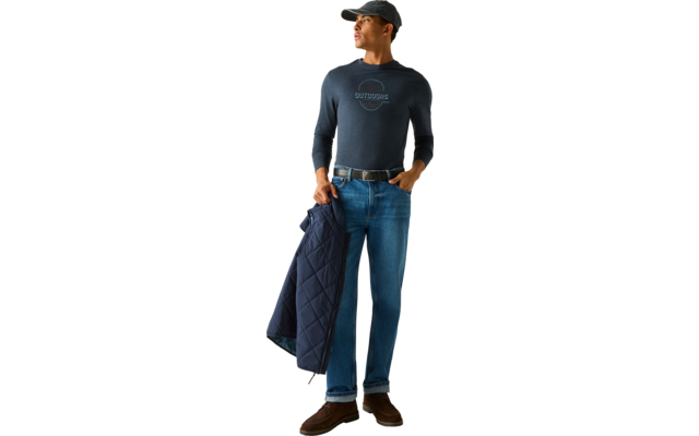 Staande man voor een lichte achtergrond, draagt een donkerblauwe baseballpet, donkerblauw lang shirt met ronde opdruk, blauwe spijkerbroek, riem en bruine schoenen, houdt een doorgestikte donkerblauwe jas in zijn linkerhand, kijkt naar rechts