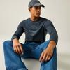Persoon zit op de vloer, draagt een grijze baseballpet, donker longsleeve met ronde opdruk en blauwe spijkerbroek, kijkt naar rechts