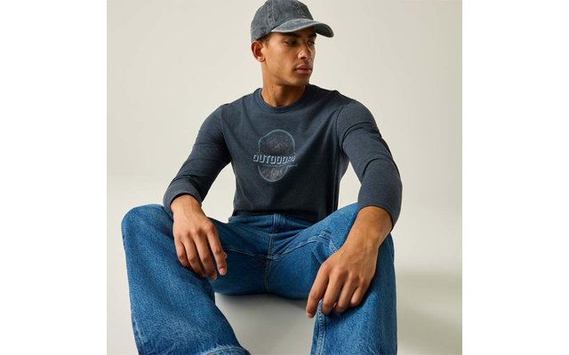 Persoon zit op de vloer, draagt een grijze baseballpet, donker longsleeve met ronde opdruk en blauwe spijkerbroek, kijkt naar rechts