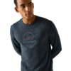 Persoon met donkerblauw longsleeve-shirt met ronde bergillustratie en de tekst 'OUTDOORS', kijkt opzij, handen achter de rug, effen lichte achtergrond