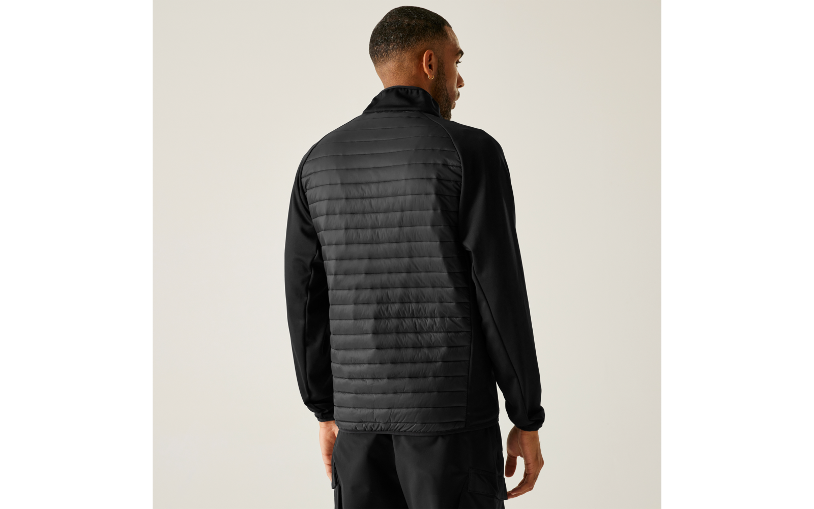 Man van achteren in een zwarte gewatteerde jas en zwarte broek voor een lichte achtergrond