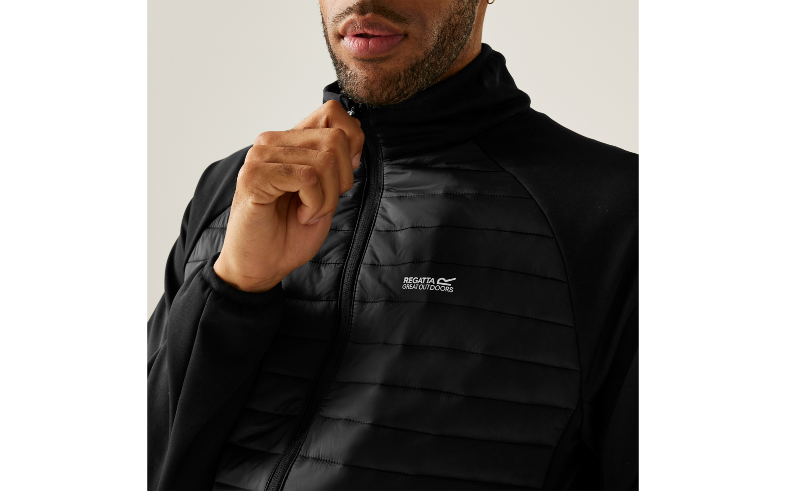 Close-up van het bovenlichaam van een persoon in een zwarte doorgestikte jas met rits, hand bij de kraag, 'Regatta Great Outdoors' logo zichtbaar op de borst