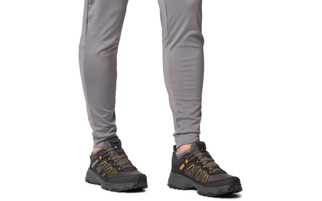 Beine mit grauer Hose und schwarzen Wanderschuhen mit orangen Details