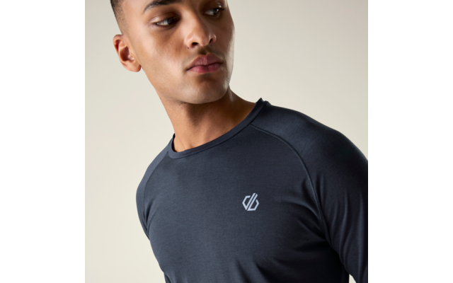 Porträt einer Person von der Brust aufwärts, trägt ein dunkles langärmliges Shirt mit kleinem weißen Logo auf der linken Brust, Blick nach links, einfarbiger heller Hintergrund