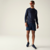Mann in Ganzkörperansicht vor hellem Hintergrund, trägt dunkelblaues langärmeliges Shirt, dunkelblaue Shorts, dunkelblaue Sportschuhe, orangefarbene Sonnenbrille und Armbanduhr
