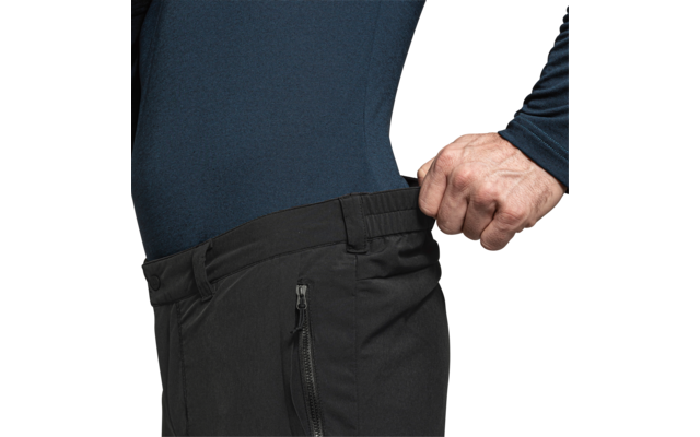 Bovenlichaam van een persoon in een donkerblauw shirt met lange mouwen, hand trekt de tailleband van een zwarte broek zijwaarts naar buiten