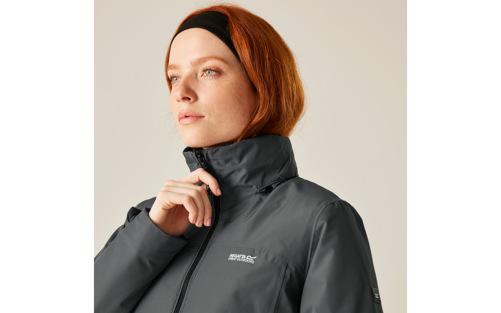 Femme aux cheveux rouges avec un bandeau noir portant une veste grise regardant vers la gauche
