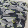 Nahaufnahme eines elastischen Bundes und einer aufgesetzten Tasche aus Stoff mit grau-schwarzem Camouflage‑Muster und neon‑grünen Akzenten, sichtbare Metall‑Öse