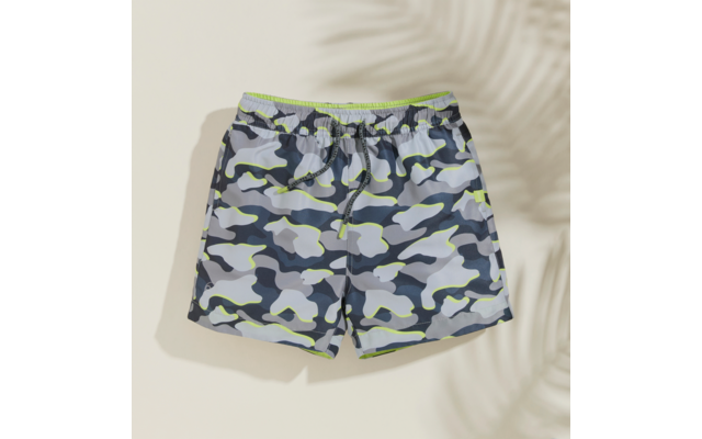 Kurze Shorts mit grau-blauem Camouflage-Muster, neon-grüner Taillenbund und Kordel, auf hellem beigen Hintergrund mit Schatten eines Palmblatts