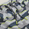 Nahaufnahme einer kurzen Hose mit elastischem Bund und grauem Camouflage-Muster mit neon-gelben Konturen, vorn sichtbare graue Kordel mit gelben Kunststoffenden