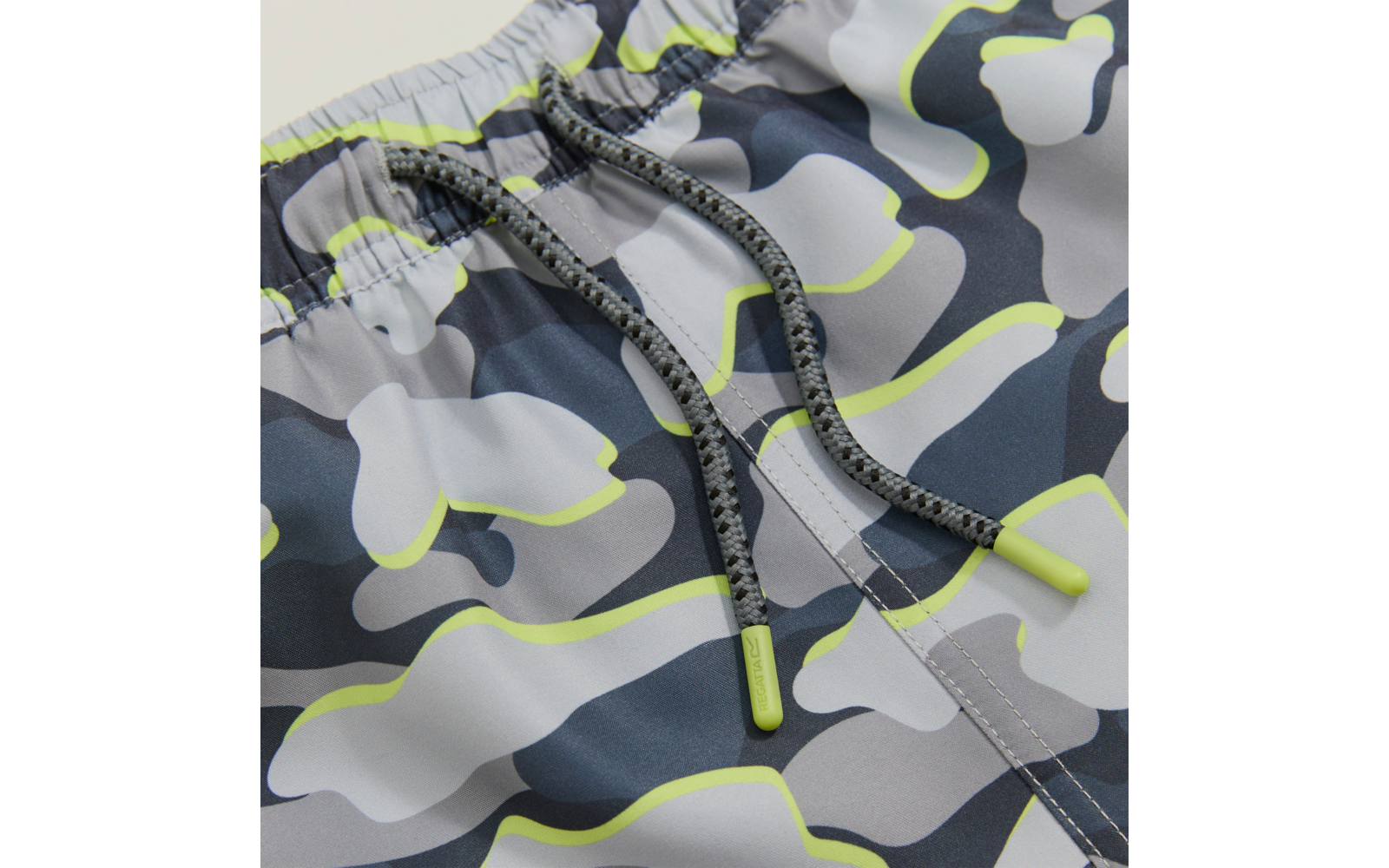 Nahaufnahme einer kurzen Hose mit elastischem Bund und grauem Camouflage-Muster mit neon-gelben Konturen, vorn sichtbare graue Kordel mit gelben Kunststoffenden