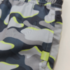 Nahaufnahme eines Kleidungsstücks mit elastischem Bund, Seitennähte, grauem und dunkelblauem Camouflage-Muster mit neongelben Akzenten, kleinem grünen Stoffetikett mit weißer Schrift
